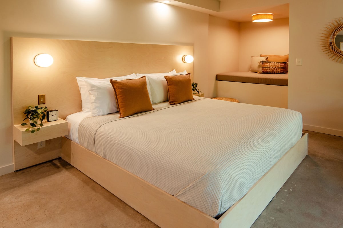 A neatly made bed with a headboard, bedside tables, and a wall-mounted mirror.
