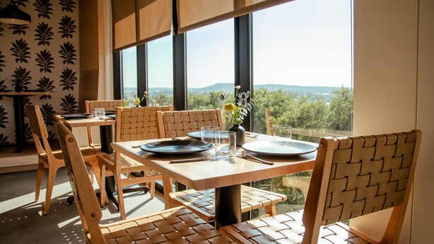 A dining area with wooden furniture and large windows offering a view of the outdoors. - Brut Hotel (Tulsa)