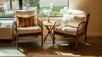 Una habitación acogedora con dos sillones de mimbre y una mesita, una planta en maceta y vistas a un jardín a través de un ventanal grande.