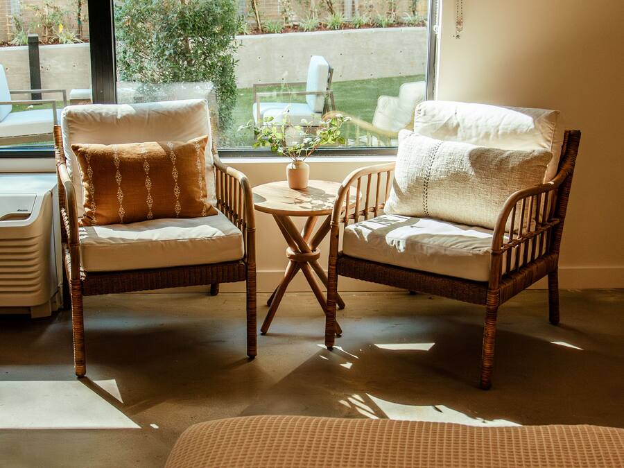Una habitación acogedora con dos sillones de mimbre y una mesita, una planta en maceta y vistas a un jardín a través de un ventanal grande.