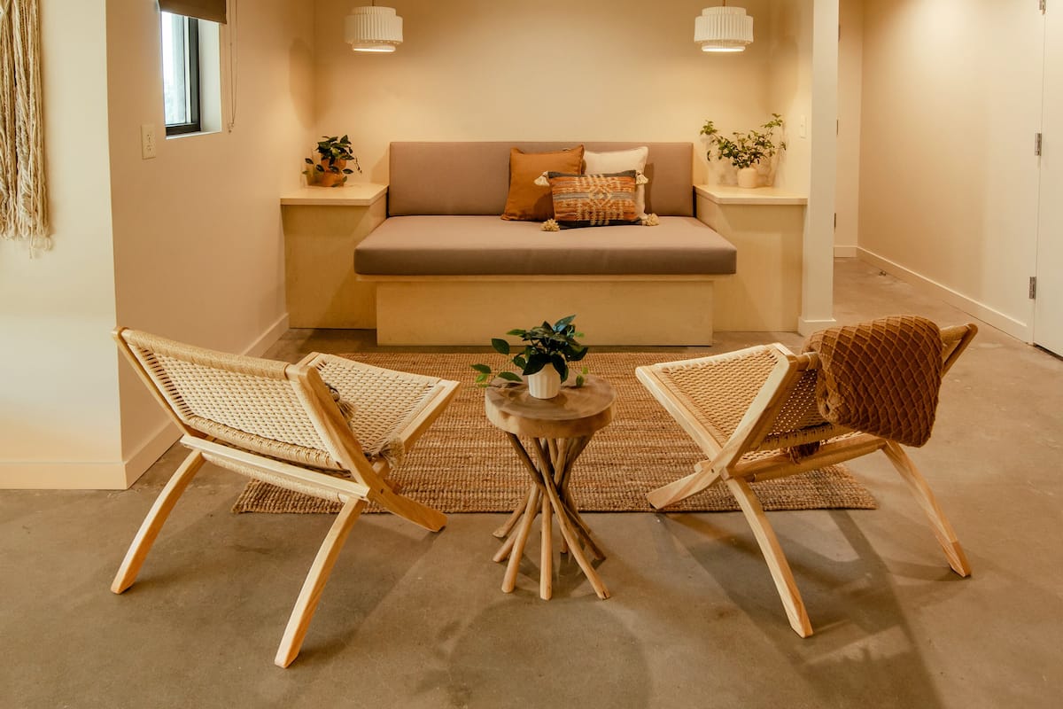 A cozy living room with a sofa, two wicker chairs, a small round table with a plant, and a window with a view.
