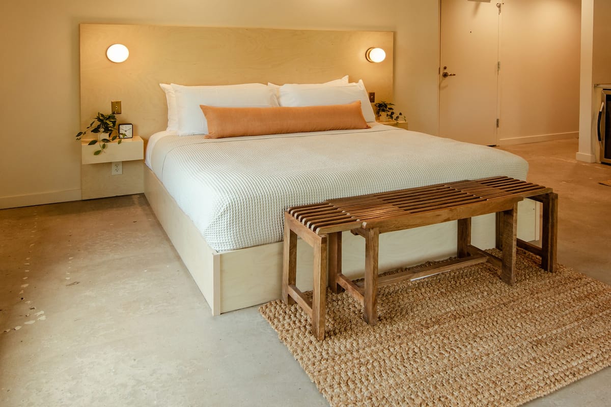 A bedroom with a bed, bedside tables, a wooden bench, and a textured rug.