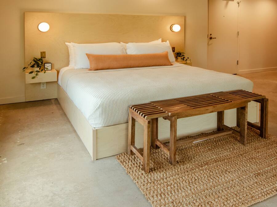 A bedroom with a bed, bedside tables, a wooden bench, and a textured rug.