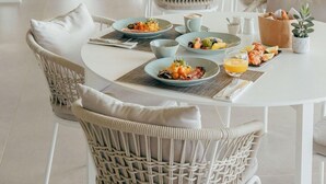 Zona pranzo con sedie e tavoli in vimini, ampie finestre e lampade a sospensione.