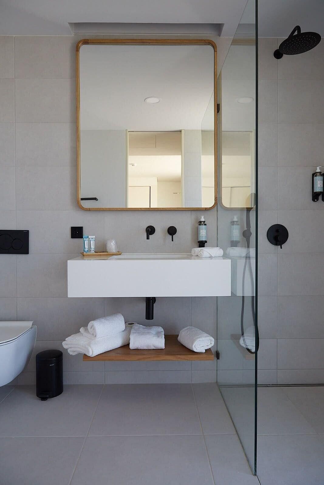 Une salle de bain moderne avec un grand miroir, un lavabo blanc et une douche à parois de verre.