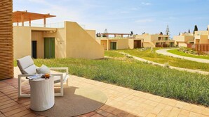 Zona relax esterna moderna con una poltrona da giardino e un tavolo, circondata da un prato curato e vialetti che conducono a un edificio con diverse unità.