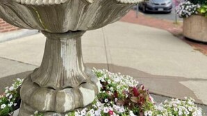 A multi-tiered stone fountain with a base surrounded by flowers.