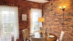 A dining area with a brick wall, round wooden table, and four upholstered chairs.