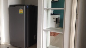 A compact kitchen with a refrigerator, white cabinetry, and a teal accent wall. - Aitalay Condotel Jomtien (Pattaya)