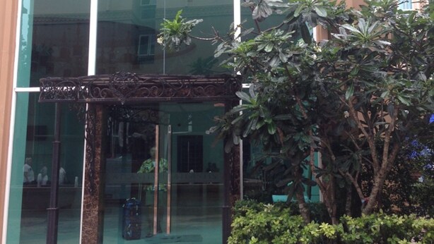 A building with a large glass entrance, a wooden pergola, and a small garden area with plants. - Aitalay Condotel Jomtien (Pattaya)