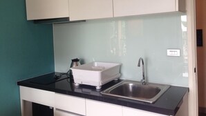 A kitchen with white cabinets, a black countertop, a white appliance, and a stainless steel sink. - Aitalay Condotel Jomtien (Pattaya)