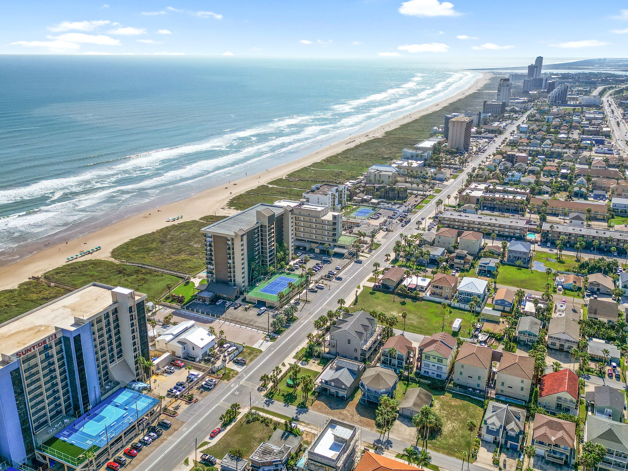 Una zona residencial costera con playa, un hotel grande con piscina y una combinación de casas unifamiliares.