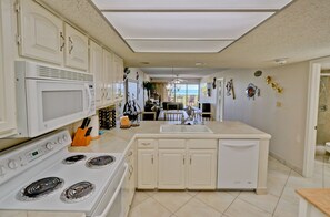 A kitchen with white cabinets, a microwave, stove, and a large island with a sink. - Ocean Vista Towers 202 (South Padre Island)