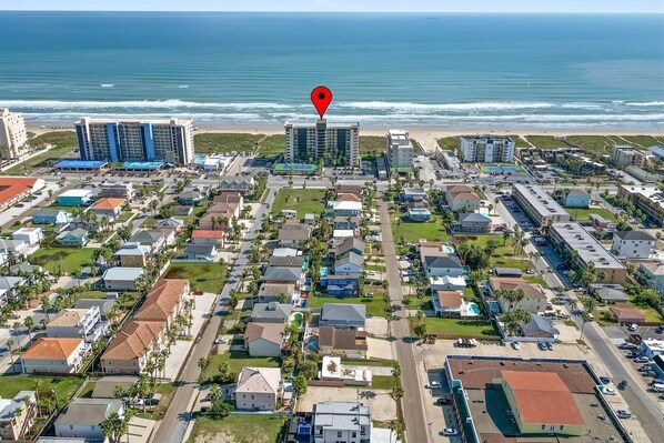 Une vue aérienne d’une zone résidentielle côtière, avec un grand hôtel en évidence, une plage et une vue dégagée sur l’océan.