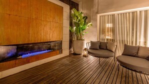 Un espace de détente moderne avec un plancher en bois, un élément décoratif aquatique intégré, une grande plante en pot et un coin salon comprenant un canapé et des fauteuils.