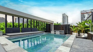 Un espace piscine aménagé sur le toit, avec un long banc, des plantes en pot et une vue sur les bâtiments de la ville.
