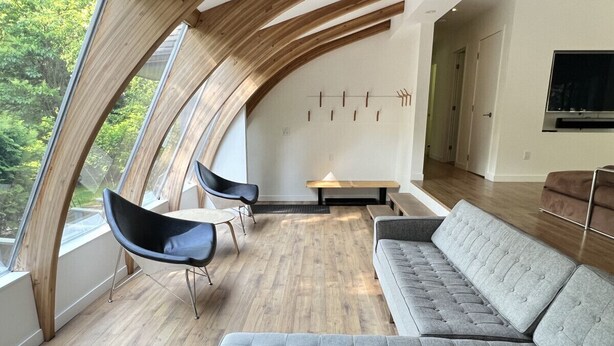A modern living room with a curved ceiling, a grey sofa, a black chair, and a small table. - Stunning Modern Beach / Ski House (Tiny)