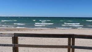 A beach with a wooden fence in the foreground and waves crashing onto the shore. - Stunning Modern Beach / Ski House (Tiny)