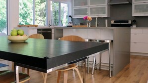 A modern kitchen with a central island, wooden chairs, and a bowl of fruit. - Stunning Modern Beach / Ski House (Tiny)