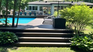 A swimming pool area with steps leading to a covered patio, surrounded by greenery. - Stunning Modern Beach / Ski House (Tiny)