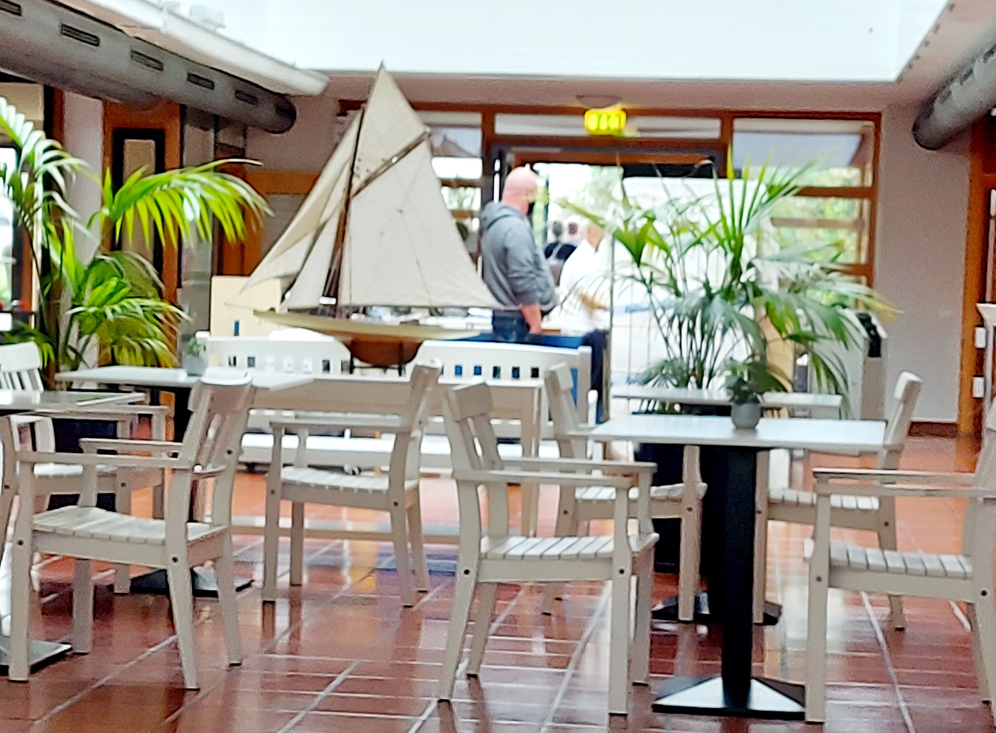 A spacious indoor area with white chairs and tables, a sailboat model, and potted plants.