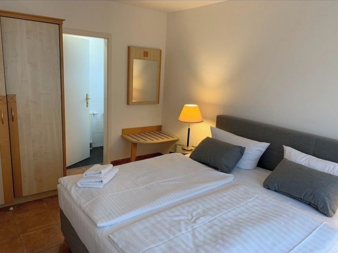 A hotel room with a large bed, a bedside table with a lamp, a wardrobe, and a mirror on the wall.