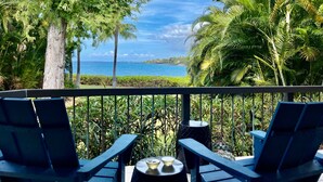 Un balcón con dos sillas y una mesita pequeña, con vistas a un paisaje tropical con palmeras y vista al océano.