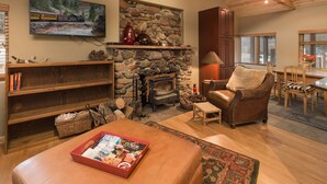 A cozy living room with a stone fireplace, wooden shelves, a leather armchair, and a dining area with a table and chairs. - ⭐️Premier Host - Serene cabin, the best amenities, north end of James Ranch  (Durango)