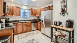 A kitchen with wooden cabinets, a stainless steel refrigerator, a coffee maker, and a toaster on a wooden table. - RED ROCKS RETREAT!  Great Location! Close to Amenities! Awesome deck with games. (Wheat Ridge)