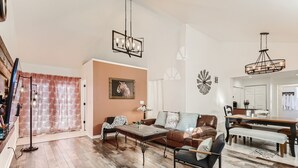 A spacious living room with a brown leather sofa, a wooden coffee table, and a dining area with a wooden bench and table. - RED ROCKS RETREAT!  Great Location! Close to Amenities! Awesome deck with games. (Wheat Ridge)