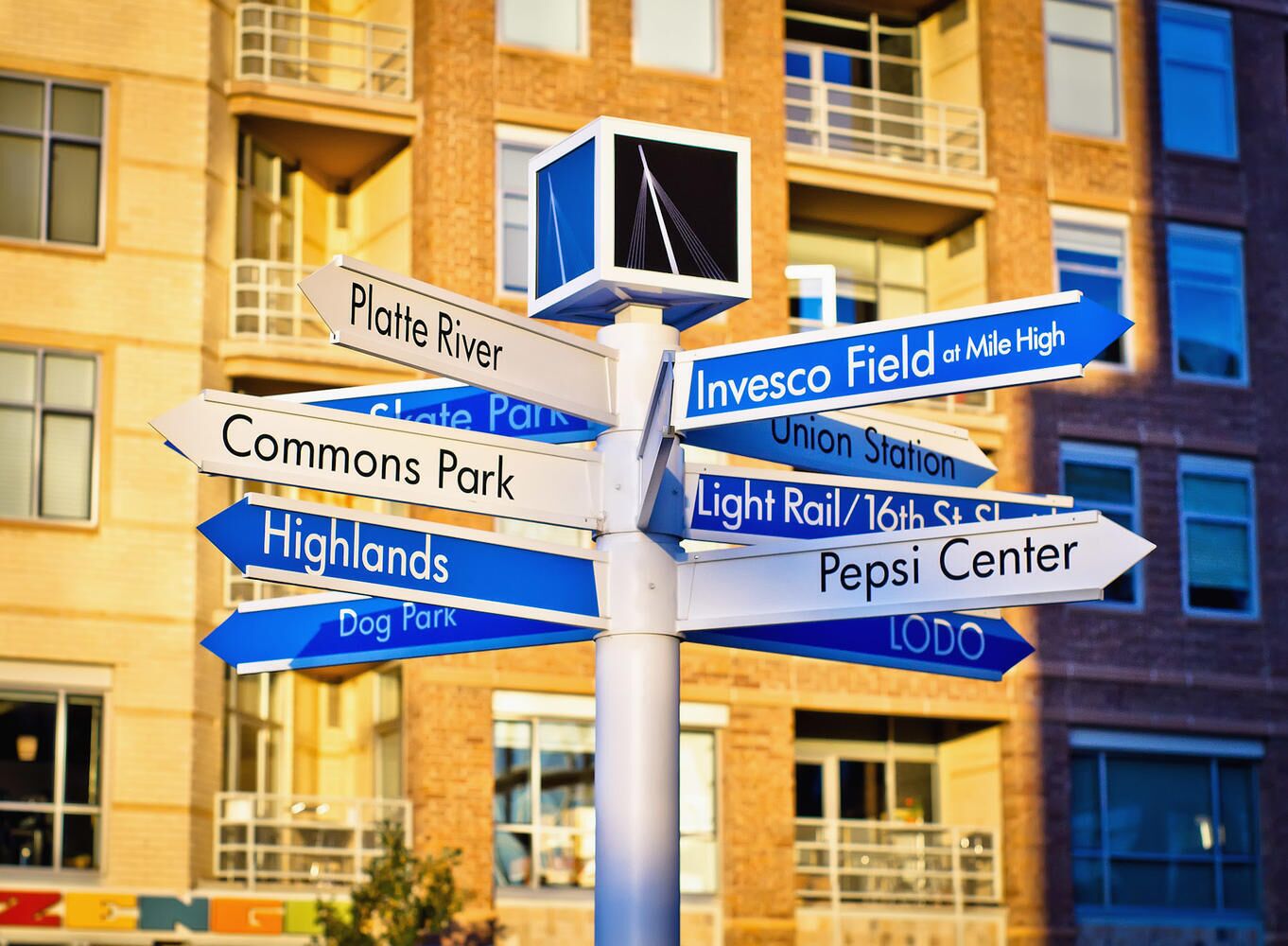 A directional sign with multiple arrows pointing to various local destinations such as Platte River, Commons Park, Highlands, Dog Park, Invesco Field, Union Station, Light Rail/16th St, Pepsi Center, and LODO.