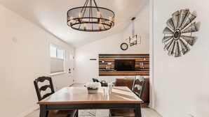 A dining area with a wooden table, chairs, and a chandelier. There is a television mounted on the wall and a decorative wall piece. - RED ROCKS RETREAT!  Great Location! Close to Amenities! Awesome deck with games. (Wheat Ridge)