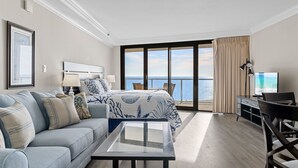A hotel room with a bed, a sofa, a desk, and a TV. The room has a large window with a view of the sea. - Book 3 Nights & Get 1 Free-See Description* Beachfront*Tram* Pool *Stunning View (Miramar Beach)