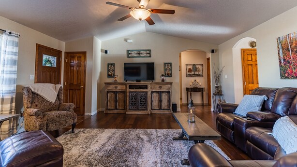 A spacious living room with a ceiling fan, a flat-screen TV, wooden cabinets, a leather sofa, and a patterned rug. - Beautiful Warm and Spacious Home, 3bed/2 full bath (Cañon City)