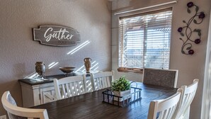 A dining area with a wooden table and white chairs, a ceiling fan, and a window with blinds. - Beautiful Warm and Spacious Home, 3bed/2 full bath (Cañon City)