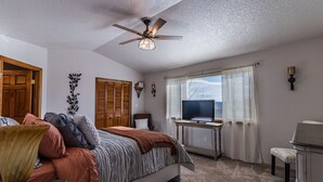 A bedroom with a bed, a ceiling fan, a TV on a stand, and a window with curtains. - Beautiful Warm and Spacious Home, 3bed/2 full bath (Cañon City)
