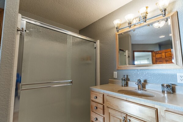 A bathroom with a glass shower door, a vanity with a sink, and a mirror with lights. - Beautiful Warm and Spacious Home, 3bed/2 full bath (Cañon City)