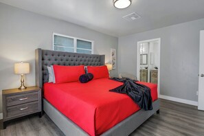 Une chambre à coucher avec un lit recouvert d’un tissu gris, une literie rouge et une table de chevet dotée de tiroirs.