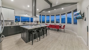 Een moderne keuken met een centraal eiland, barstoelen en een eethoek met rode stoelen.