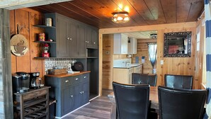 A rustic kitchen with wooden cabinets, a coffee machine, and a dining area with a table and chairs.