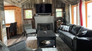 A cozy cabin interior with a fireplace, a sofa, a dining table with chairs, and a television mounted on the wall.