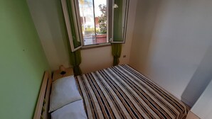 Ein kleines Zimmer mit einem Bett, einem Fenster und einem grünen Vorhang.