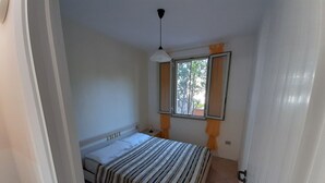 Une chambre à coucher avec un lit, une fenêtre avec des rideaux, une table de chevet et un luminaire au plafond.