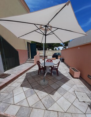 A patio area with a table and chairs under a large umbrella, a tiled floor, and a car parked in the background.