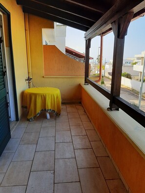 Un balcó amb taula groga, terra de rajola i vista al carrer.