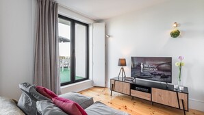 A modern living room with a large TV, a wooden cabinet, and a view of the outdoors. - GuestReady - One Step Closer (Porto)