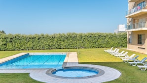Une piscine rectangulaire avec un jacuzzi, entourée d’une pelouse et de chaises longues.