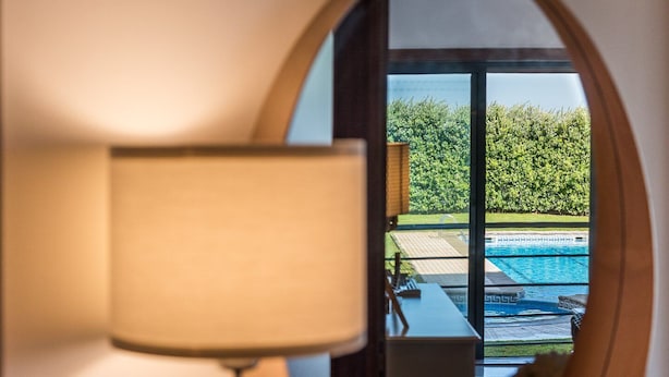 Une vue à travers une fenêtre, avec une lampe, donnant sur une piscine et de la verdure.