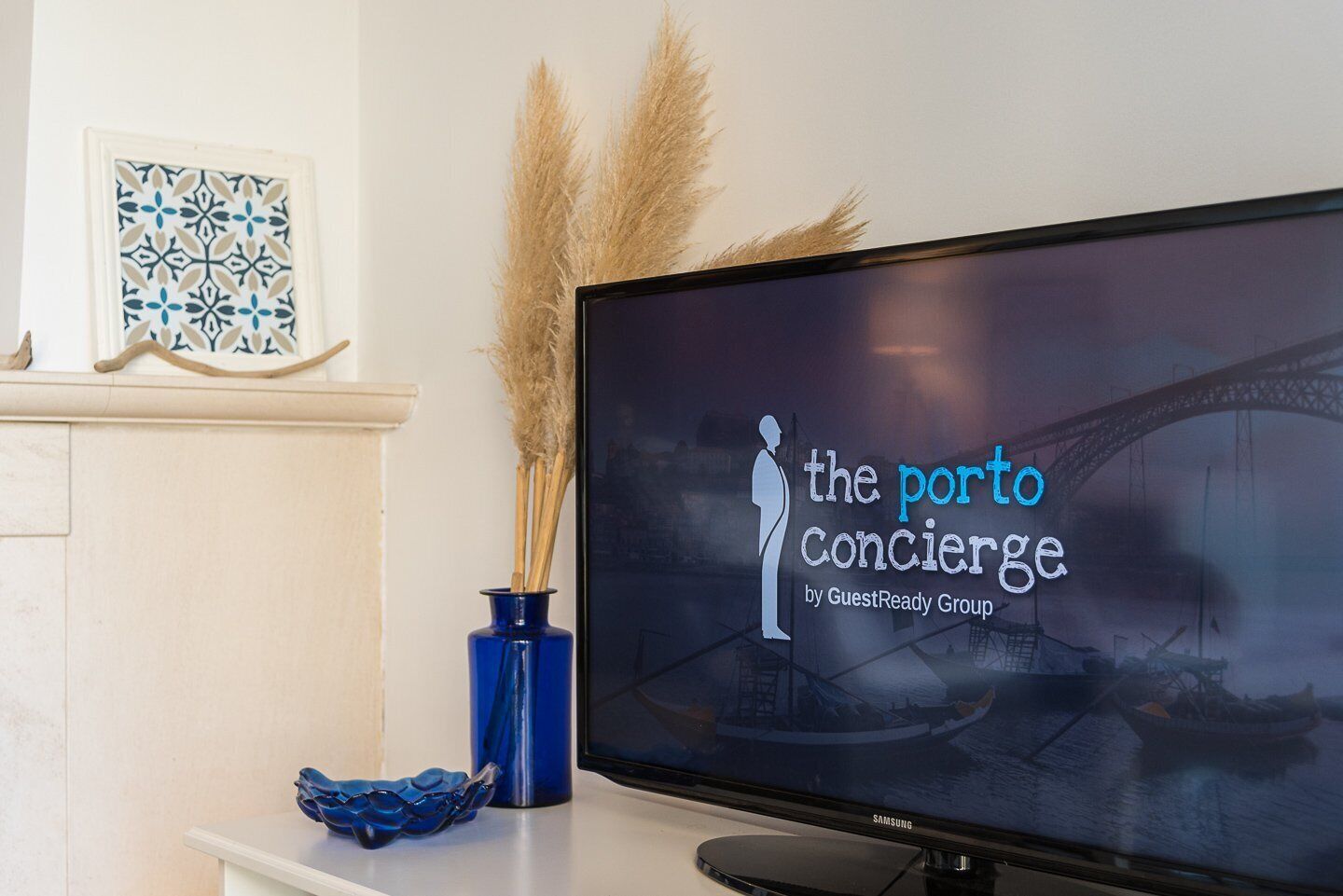Un televisor mostrando 'The Porto Concierge by GuestReady Group', con un puente y barcos al fondo.