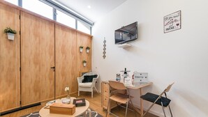 Une chambre moderne avec une armoire en bois, un téléviseur, un bureau avec une chaise et un panneau accroché au mur.